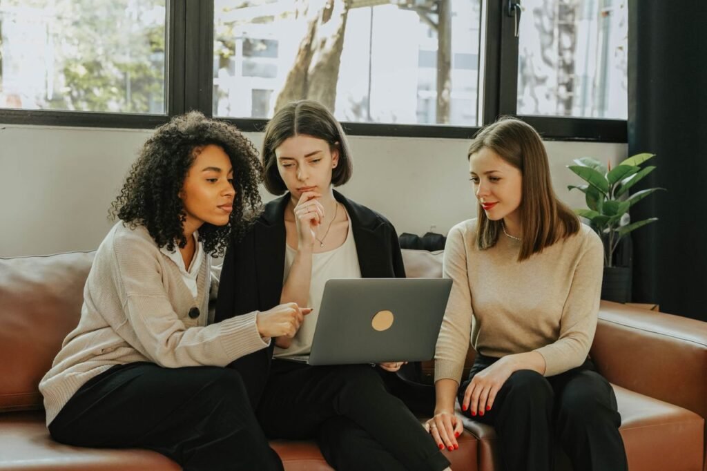 Three women working together on a laptop indoors. Teamwork and collaboration.